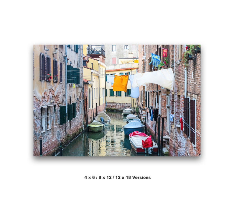 May include: A narrow canal in Venice, Italy, with colorful buildings lining the sides.  Laundry hangs on lines strung across the canal.  Several small boats are moored in the water.