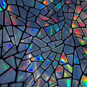 May include: A close-up of iridescent fabric with a geometric pattern of silver-toned, irregularly shaped pieces. The fabric has a black background and the pieces are outlined in black.