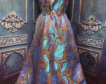 Könnte beinhalten: Ein trägerloses, bodenlanges Kleid aus lebhaftem, schillerndem Stoff mit einem wirbelnden Muster in Metallic-Gold, Magenta und leuchtendem Blau. Das Kleid ist in der Taille mit einem dekorativen Gürtel aus ineinandergreifenden Metallringen gerafft.