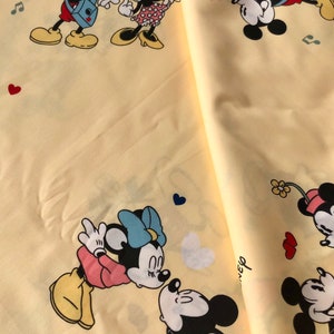 May include: Yellow fabric with a repeating pattern of Mickey Mouse and Minnie Mouse. The pattern includes Mickey Mouse playing a guitar, Minnie Mouse dancing, and Mickey and Minnie kissing. The fabric also has hearts, musical notes, and flowers.