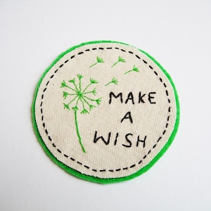 May include: A round, green and white embroidered patch with a dandelion and the text "MAKE A WISH".