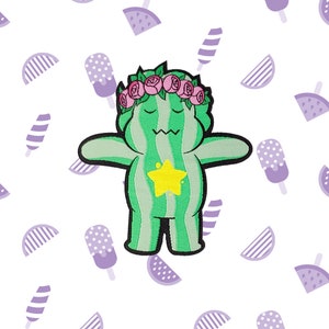 May include: Green watermelon character with a yellow star on its chest and a pink flower crown. The character has outstretched arms and a friendly expression.