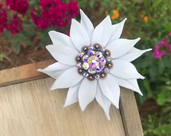 May include: A white leather flower with a crystal center. The flower is on a wooden surface.