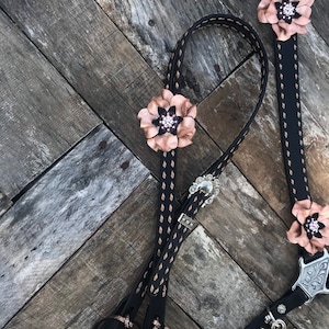 Puede incluir: Riendas de caballo de cuero negro con detalles y costuras en oro rosa. Las riendas tienen un diseño floral decorativo con pedrería.