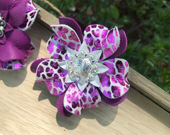 May include: Two purple leather flowers with white and pink leopard print accents. The flowers have silver and rhinestone embellishments.