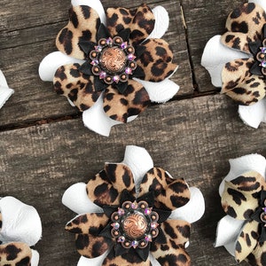 May include: Five white leather flower shapes with brown and black leopard print fabric centers. Each flower has a decorative copper and crystal embellishment in the center.