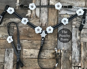 May include: Black and white horse tack set with white flower accents. The set includes a breast collar, reins, and a lead rope. The breast collar has a silver buckle and the reins have a silver buckle and a silver concho. The lead rope has a silver concho. The text "The Punchy Posey" is visible in the image.
