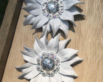 May include: Two white leather flower shapes with silver and crystal embellishments. Each flower has a silver center with a swirl design and is surrounded by a circle of clear crystals.