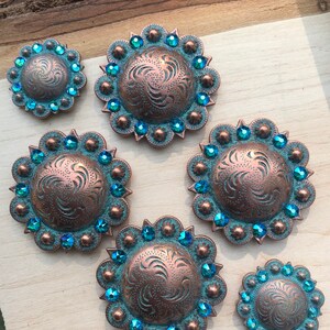 Könnte beinhalten: Sechs runde, kupferfarbene Metall-Conchos mit einem Wirbeldesign und türkisblauen Strasssteinen an den Rändern.