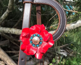 May include: A brown leather horse halter with a red leather flower accent. The flower has a copper-toned metal center with turquoise rhinestones.