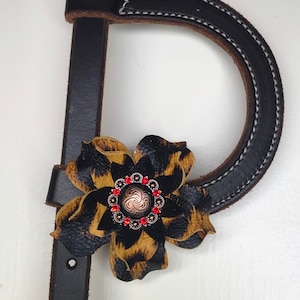 May include: A black leather halter with a brown and black leopard print flower accent. The flower has a red rhinestone center.