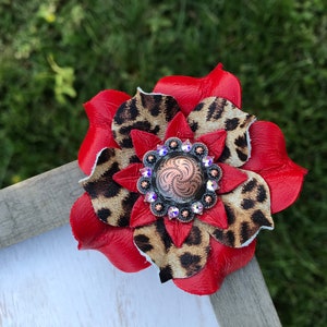 May include: A red and brown leather flower with a rhinestone and copper concho in the center.
