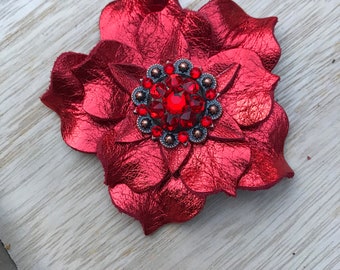 May include: A red leather flower with a jeweled center. The flower is made of multiple petals and has a metallic sheen.
