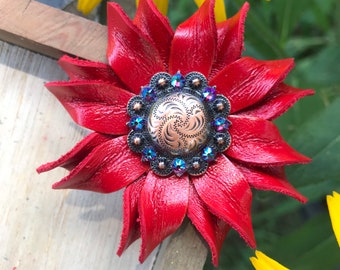 May include: A red leather flower with a copper and silver concho in the center. The concho is surrounded by blue rhinestones.