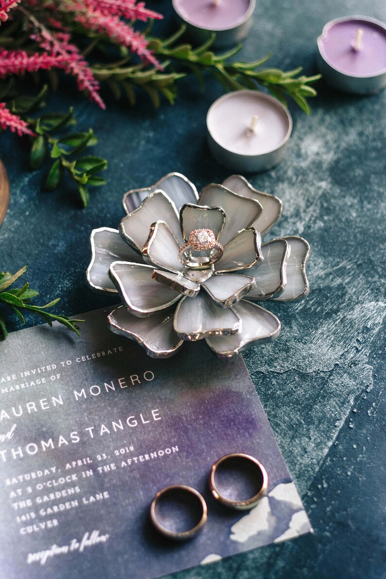 Blue stained-glass flower ring dish showcased with lavender candles and a wedding invitation in a romantic editorial flatlay. The soft color harmony highlights the engagement ring and complements invitation styling, engagement shoots, and refined bridal-party gifting moments.