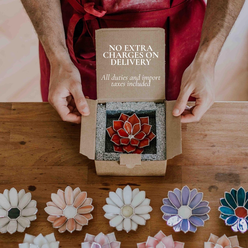Puede incluir: Una suculenta de vidrio rojo y naranja en una caja de cart&oacute;n, con el texto "NO EXTRA CHARGES ON DELIVERY" y "All duties and import taxes included". Debajo hay varios posavasos de flores de vidrio de colores.