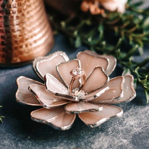 Handcrafted soft blush stained-glass flower ring dish holding a delicate engagement ring, styled with a copper vessel and botanical greenery. Soft-glam, vintage-romantic wedding aesthetics framed in an editorial flatlay, ideal for bridal morning details and elegant keepsake gifting.