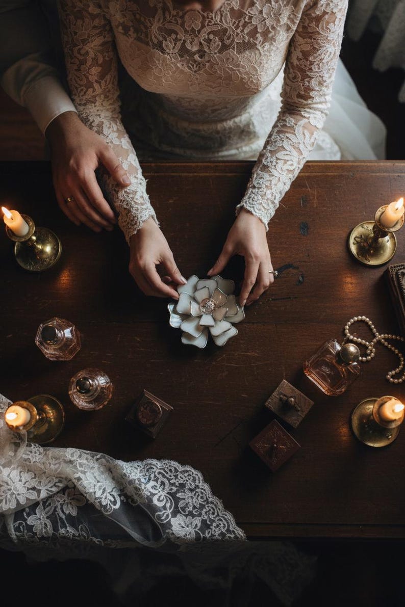 Puede incluir: Un letrero de madera r&uacute;stico blanco con la palabra "Welcome" escrita a mano. El letrero tiene un aspecto envejecido y un elemento floral decorativo. El fondo es una imagen borrosa de una casa.