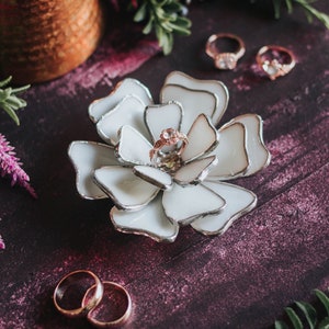Cream stained-glass flower ring dish styled on a rich plum background with soft botanical textures and lavender tealights. The soft-glam palette elevates the engagement ring, fitting modern romantic editorials, invitation flatlays, and luxury bridal aesthetics.