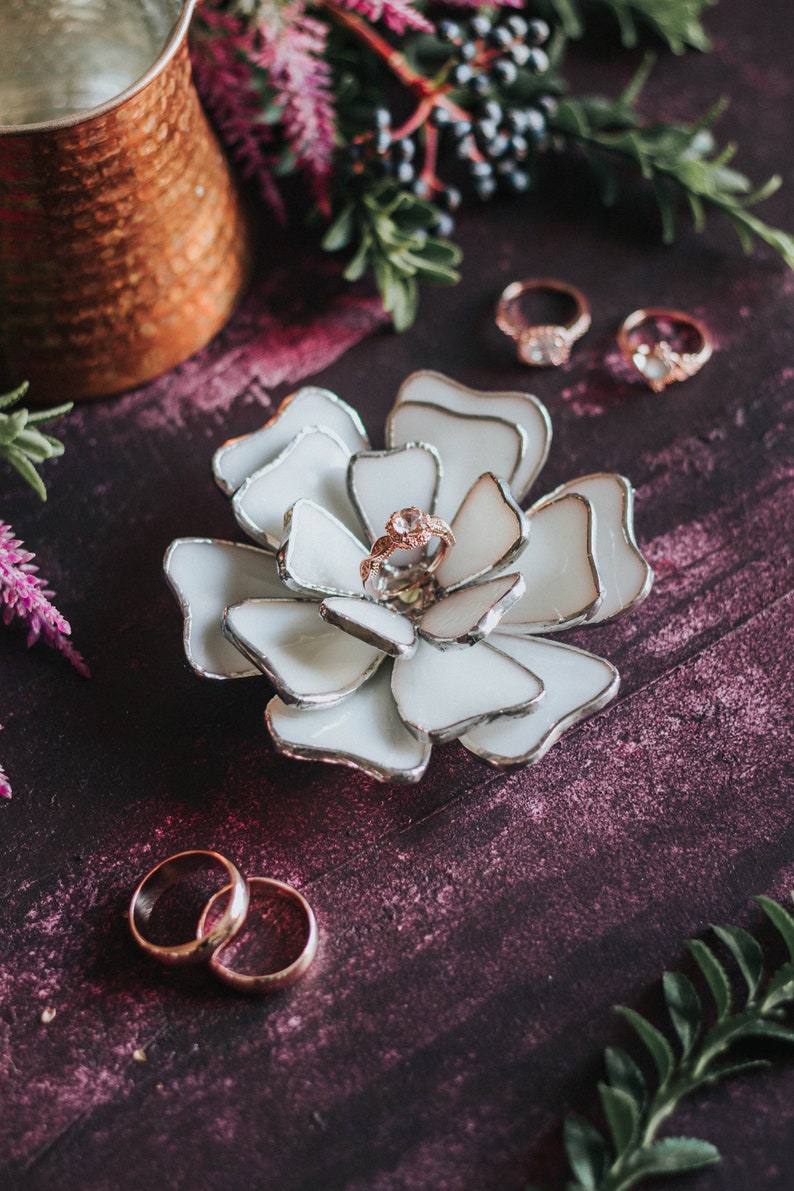 Cream stained-glass flower ring dish styled on a rich plum background with soft botanical textures and lavender tealights. The soft-glam palette elevates the engagement ring, fitting modern romantic editorials, invitation flatlays, and luxury bridal aesthetics.