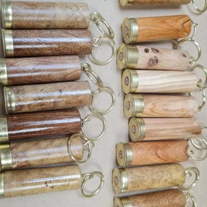 May include: A selection of wooden keyrings with brass-coloured ends and key rings. The keyrings are crafted from diverse wood types, displaying varied grain patterns and colours, from light to dark brown.