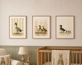Può includere: Tre stampe da parete incorniciate con illustrazioni ad acquerello di anatre. La stampa a sinistra mostra una singola anatra su righe verticali. Quella centrale raffigura tre anatre tra erbe alte. Quella a destra mostra un'anatra con tre anatroccoli.