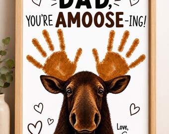 Può includere: Una stampa incorniciata con l'illustrazione di un alce marrone che ha due impronte di mani marroni come corna. Il testo recita DAD, YOU'RE AMOOSE-ING! e Love, Gus. Il design include cuori neri su sfondo bianco in una cornice di legno chiaro.