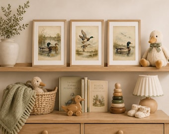 May include: Three framed prints of mallard ducks in natural settings, a plush duck toy with a green bow, a woven basket with a small duck toy, a wooden duck pull toy, two books titled The Tale of Jemima Puddle-Duck and Beatrix Potter, a wooden stacking toy, and a lamp.