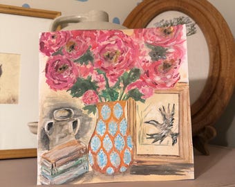Può includere: Un dipinto quadrato ad acquerello che raffigura un vivace bouquet di fiori rosa in un vaso con motivi arancioni e blu. A sinistra, una pila di libri è posizionata accanto a una brocca grigia. A destra, un'illustrazione incorniciata mostra un uccello.