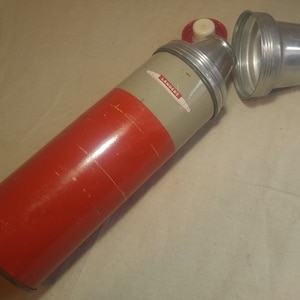 Puede incluir: Un termo de metal rojo y gris con una tapa plateada. El termo tiene una etiqueta que dice "Landers".