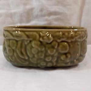 Pode incluir: Um vaso oval de cerâmica verde com um design floral em relevo.