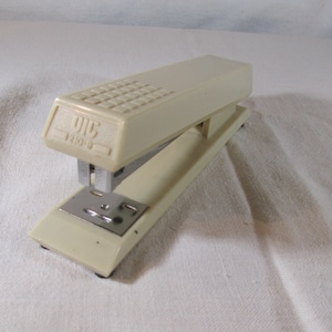 May include: A white plastic stapler with a silver staple remover and a black base. The stapler has a textured top and the text "DIC 110-5" printed on the front.