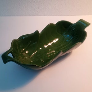 Puede incluir: Un plato de servir de cerámica verde con forma de hoja y dos asas.