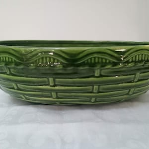 May include: A large, green ceramic bowl with a woven basket design. The bowl has a scalloped rim and is ideal for serving salads, fruit, or other dishes.