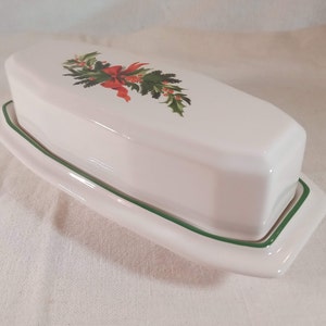 May include: White ceramic butter dish with a green rim and a festive holly and red bow design.