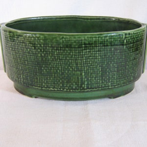 Puede incluir: Una maceta de cerámica verde con un patrón tejido. La maceta tiene una forma ovalada redondeada y un borde ancho.
