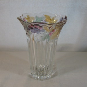 May include: A clear glass vase with a scalloped rim and a grapevine design. The vase has a textured, ribbed surface and features multi-colored grapes and leaves.