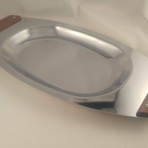 以下が含まれることがあります： 木製の取っ手が2つ付いた銀製のサービングトレイ。トレイは楕円形で、わずかに盛り上がった縁があります。