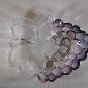 May include: A clear glass bowl shaped like a bunch of grapes with a frosted butterfly design. The grapes are a light purple color.