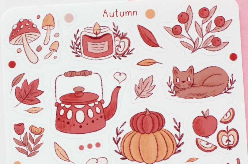 May include: A set of autumn-themed stickers featuring a red teapot, a pumpkin, a cat, a candle, mushrooms, leaves, and apples. The stickers are on a white background and have a hand-drawn style.