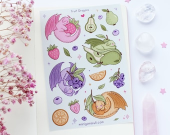 Puede incluir: Una hoja de pegatinas con dragones con temática de frutas. Las pegatinas están sobre un fondo azul claro con contornos blancos. Los dragones están acurrucados dentro de una pera, una naranja, una fresa y un arándano. El texto "Fruit Dragons" está en la parte superior de la hoja.