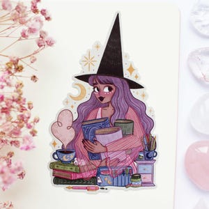 Peut inclure: Un autocollant découpé représentant une illustration d'une personne aux longs cheveux violets portant un chapeau de sorcière noir pointu. Le personnage tient plusieurs livres et est entouré d'une tasse fumante, de livres empilés et de papeterie.