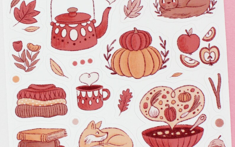 May include: A set of autumn-themed stickers featuring illustrations of a teapot, a pumpkin, a bowl of soup, a fox, a sweater, a mug of hot cocoa, and apples. The stickers are in shades of red, orange, and brown.