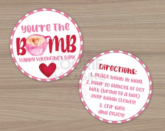 Puede incluir: Dos pegatinas redondas con temática de San Valentín. Una pegatina tiene el texto "you're the BOMB" con una taza de café rosa y un corazón rojo. La otra pegatina tiene instrucciones.