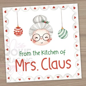 May include: A white card with a red scalloped border. The card features a cartoon illustration of Mrs. Claus with a red and green ornament hanging above her head. The text "From the Kitchen of Mrs. Claus" is written in red and green.