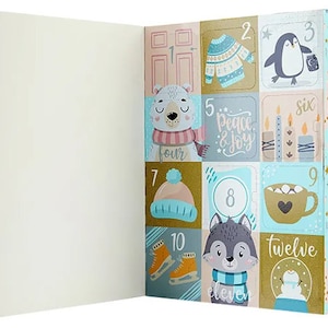 May include: A festive Advent calendar with a light blue and gold design. The calendar features numbered squares with winter-themed illustrations, including a penguin, polar bear, and a cup of hot cocoa. The calendar is open, revealing a blank interior.
