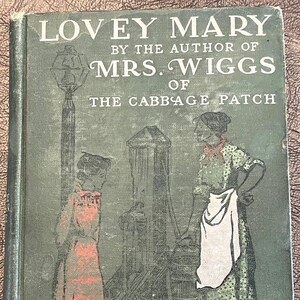 May include: Antique book cover of "Lovey Mary" by Alice Hegan Rice. The cover is a muted green with illustrations of two women and a water pump. The title and author's name are in white lettering.