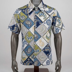 May include: A short-sleeved button-down shirt featuring a diamond-patterned paisley print in shades of blue, olive green, and white. The collar is pointed, and a tag at the neck displays the text SIZE SMALL (MEN'S). The shirt is displayed on a mannequin.
