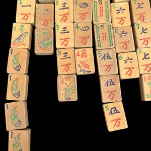 May include: A collection of rectangular wooden Mahjong tiles arranged in columns. Each tile features hand-painted Chinese characters in red, blue, and green ink, along with numerical indicators and illustrations of bamboo stalks on specific tiles.
