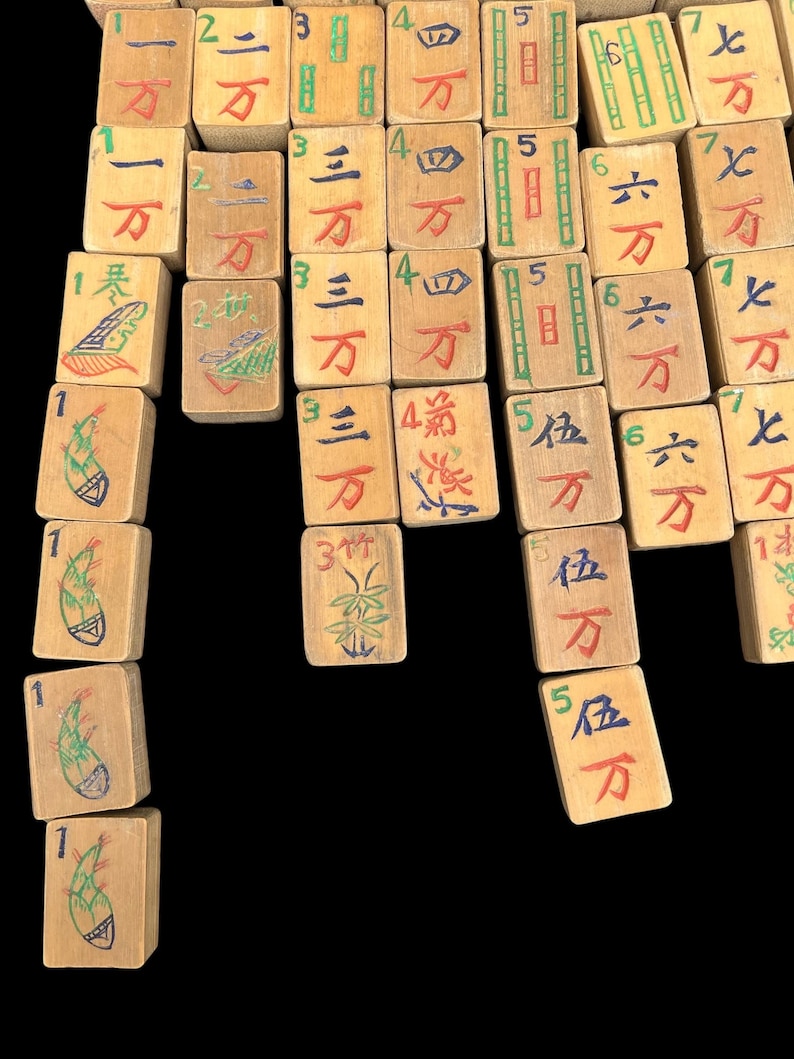 May include: A collection of rectangular wooden Mahjong tiles arranged in columns. Each tile features hand-painted Chinese characters in red, blue, and green ink, along with numerical indicators and illustrations of bamboo stalks on specific tiles.
